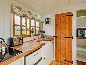 A kitchen with wooden countertops, a sink, a stove, and a refrigerator. There are large windows with a view of greenery outside. - 1 Bed in Market Rasen (oc-83847) (Faldingworth)