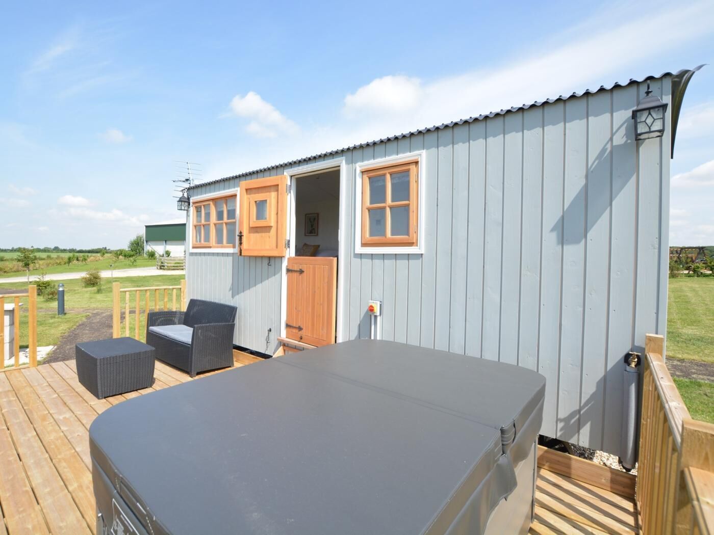A small, light blue metal building with a deck, two windows with wooden shutters, and a covered outdoor seating area.