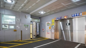 An elevator area with a metallic elevator door, a yellow safety line on the floor, and various informational signs on the walls.