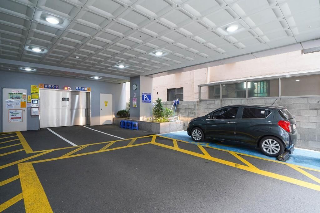 Un estacionamiento con un coche, una máquina expendedora y un letrero azul que indica disponibilidad de estacionamiento.
