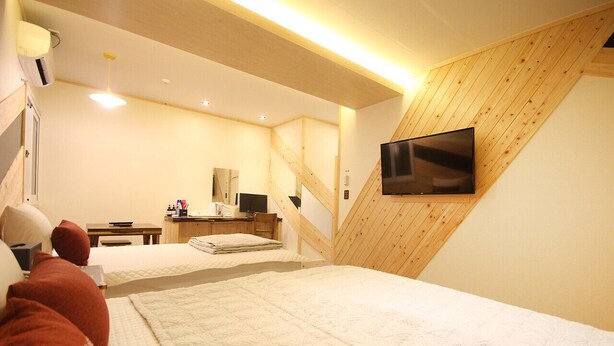 A bedroom with two beds, a TV mounted on the wall, and a wooden sloped ceiling.