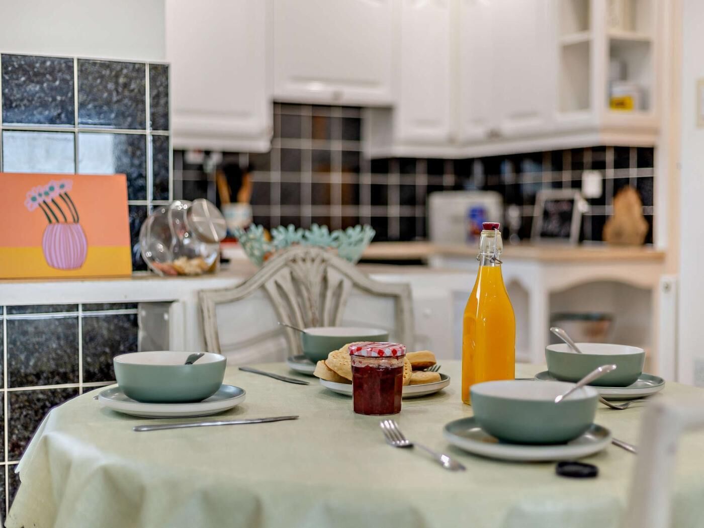 A dining table with bowls, a bottle of juice, and a painting on the wall.