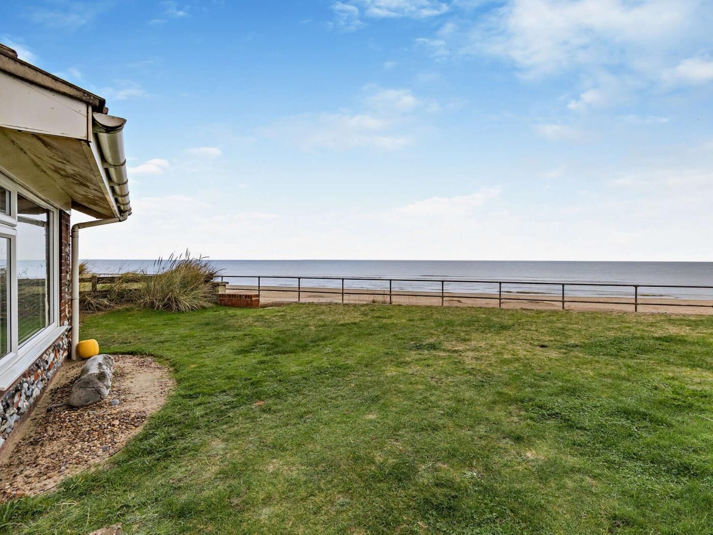 A coastal property with a grassy lawn, a concrete deck, and a view of the sea.