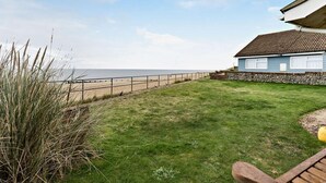 En fastighet vid kusten med en gräsklädd gräsmatta, en stenmur och utsikt över stranden.