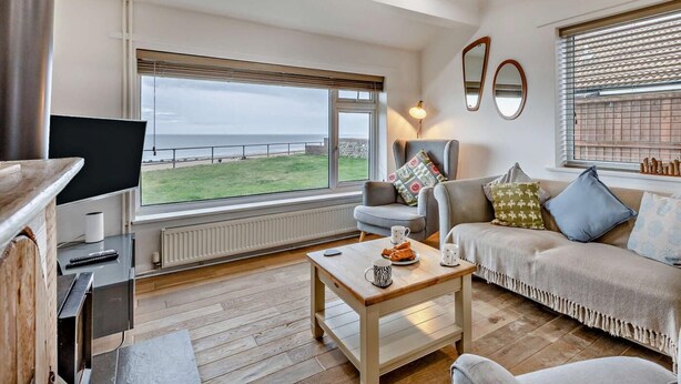 Ett vardagsrum med en TV, en soffa, ett soffbord och utsikt över havet.