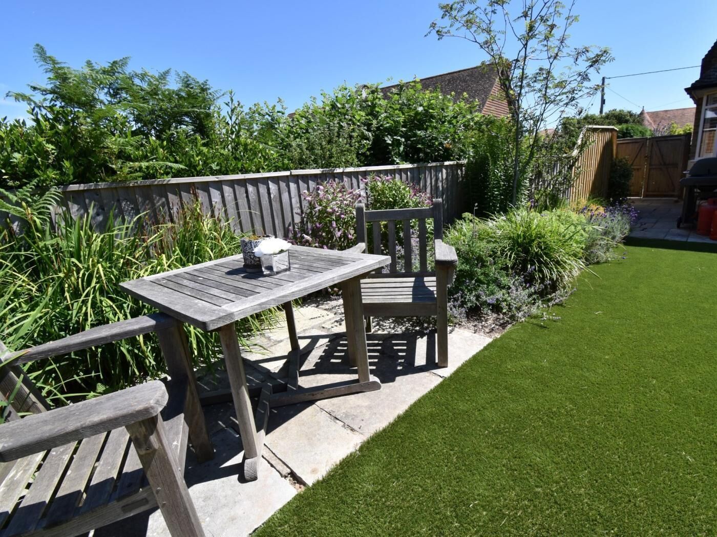 Een terras met een tafel en stoelen, omgeven door een verzorgd gazon en verschillende planten.