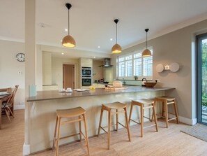A modern kitchen with a central island, wooden stools, pendant lighting, and a view of the outdoors. - 5 Bed in Swanage (oc-dc030) (Studland)