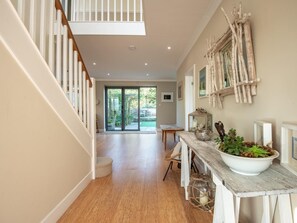 A spacious interior with a wooden staircase, a dining area with a rustic table, and a view of a garden through glass doors. - 5 Bed in Swanage (oc-dc030) (Studland)