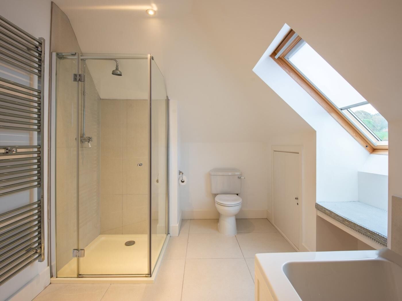 A modern bathroom with a glass-enclosed shower, a toilet, and a skylight.
