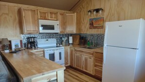 A kitchen with wooden cabinets, a microwave, a stove, a sink, and a refrigerator. - Alpha Wolf Cabin at the Wolf Haven Cabins (Lovell)