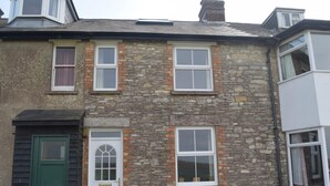 Une maison en pierre à deux étages, avec une porte verte, des fenêtres à cadre blanc et une petite fenêtre de grenier.