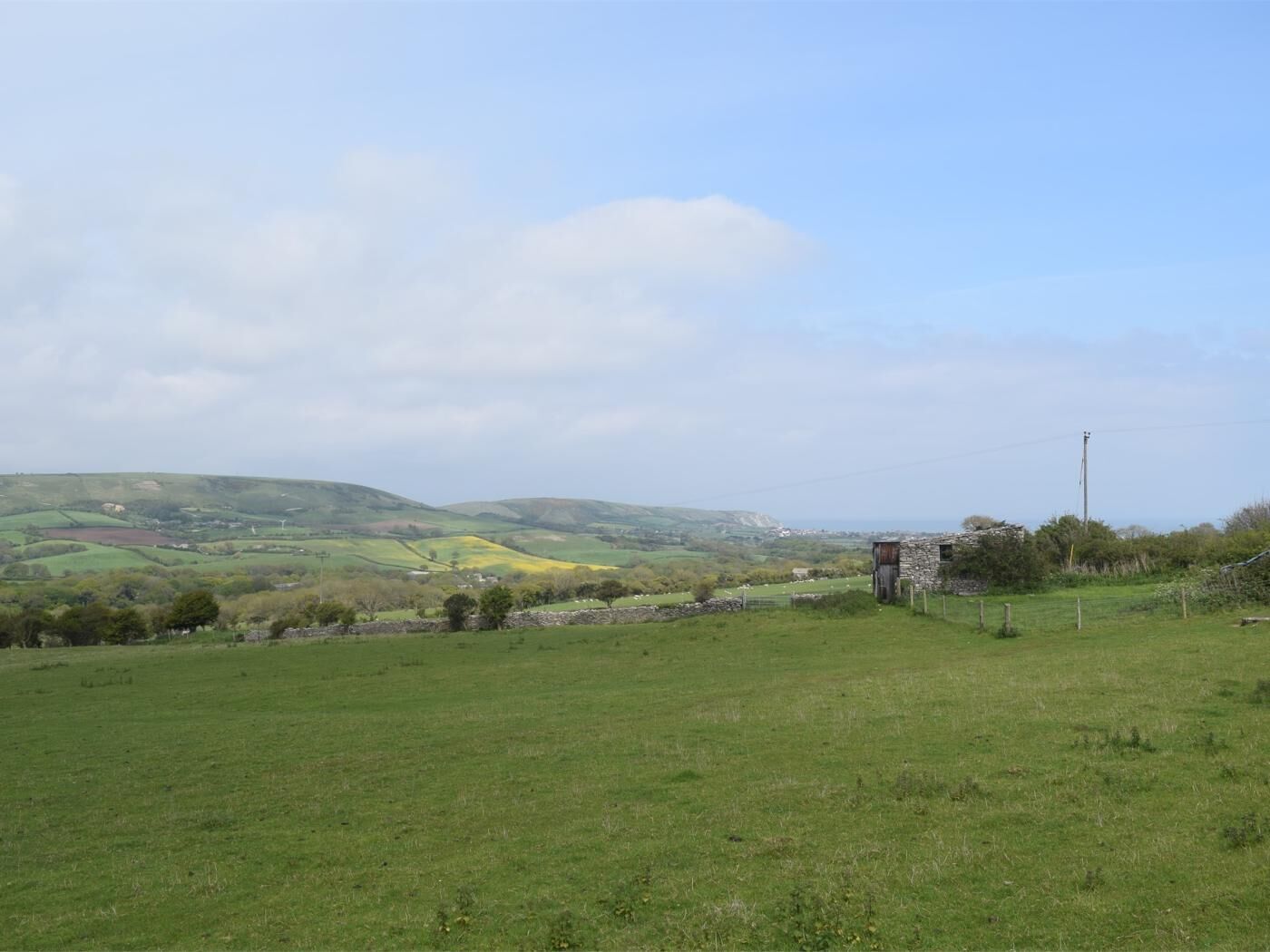 Paisagem rural com colinas onduladas, uma construção de pedra e céu claro.