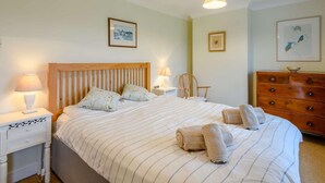 Un lit bien fait, avec une literie à rayures, une tête de lit en bois, deux tables de chevet avec des lampes, une commode en bois et des œuvres d’art encadrées accrochées aux murs.