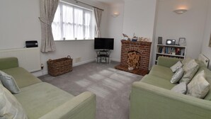 A living room with two green sofas, a fireplace, a television, and a bookshelf. - 3 Bed in Swanage (oc-dc072) (Studland)