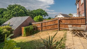 A fenced backyard with a brick structure, a wooden fence, and a patio with outdoor furniture. - 3 Bed in Swanage (oc-dc072) (Studland)