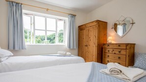 A bedroom with two beds, a wooden wardrobe, a mirror, and a window with curtains. - 3 Bed in Swanage (oc-dc072) (Studland)