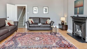 A living room with a dark leather sofa, a patterned rug, a fireplace, and framed pictures on the wall. - 3 Bed in Portland (oc-dc031) (Portland)