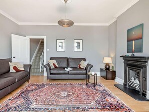 Ein Wohnzimmer mit einem dunkelbraunen Ledersofa, einem gemusterten Teppich, einem Kamin und gerahmten Bildern an der Wand.