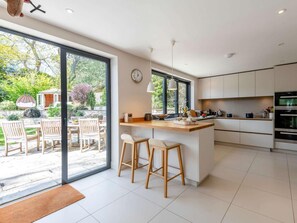 Een moderne keuken met een groot eiland, barkrukken en uitzicht op de tuin.