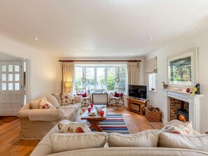 Ein Wohnzimmer mit einer Sofagarnitur, einem Couchtisch, einem Fernseher, einem Kamin und einem großen Fenster mit Vorhängen.