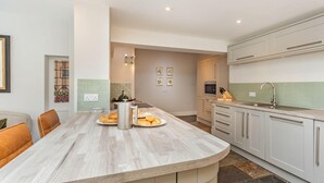 A modern kitchen with a curved island, white cabinetry, and a stone backsplash. - 9 Bed in Keswick (oc-sz238) (Keswick)