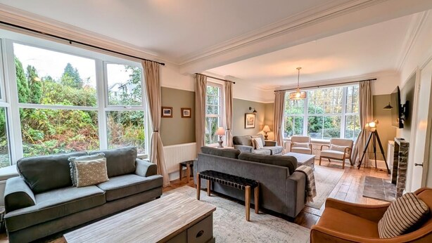A spacious living room with large windows, a sofa set, a coffee table, and a dining area. - 9 Bed in Keswick (oc-sz238) (Keswick)