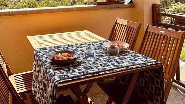 En terrass med ett bord dukat för två personer, en krukväxt och utsikt över bergen.