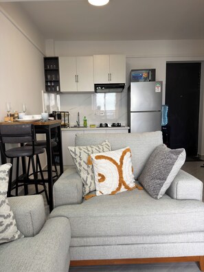 A modern living room with a grey sofa, a dining table with chairs, a kitchen area with white cabinets and appliances, and a water dispenser. - Marvelous 1-bedroom apartment in vibrant Nairobi perfect for your stay (Nairobi)