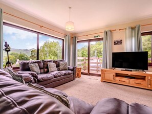 Ein Wohnzimmer mit Sofa, Fernseher und einem Balkon mit Blick.