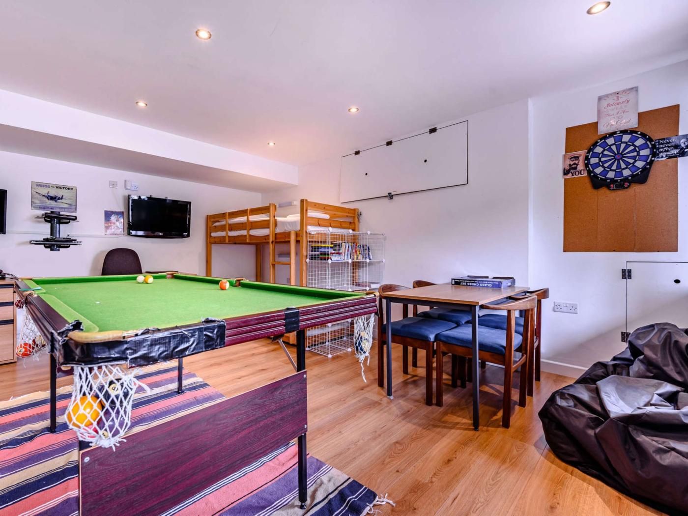 A pool table with a net, a dartboard, a television, and a bunk bed.