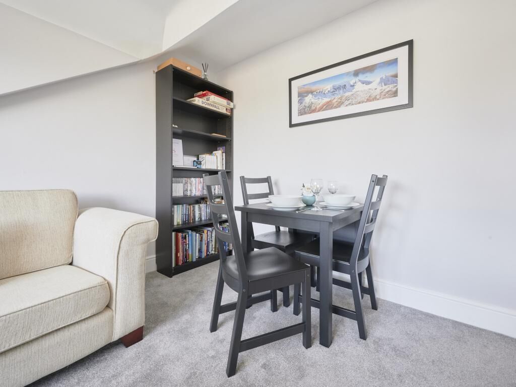 Een kamer met een bank, een eettafel met stoelen, een boekenkast en een lijst aan de muur.