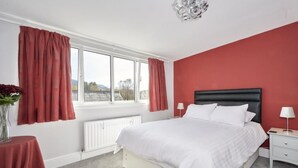 Un dormitorio con cama, mesita de noche, lámpara, ventana con cortinas y radiador.