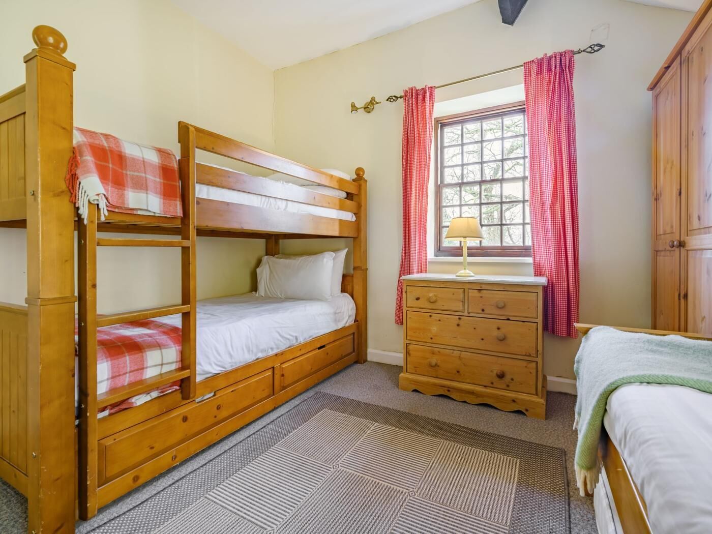 Een slaapkamer met een stapelbed, een dressoir en een raam met gordijnen.
