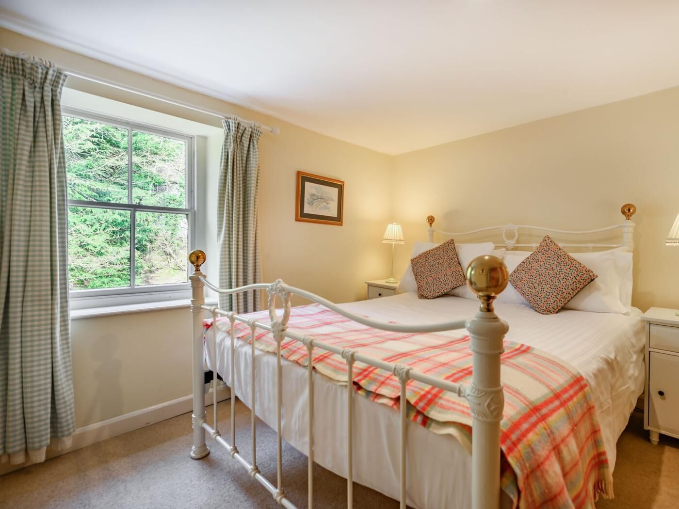A bedroom with a bed, nightstands, a window with curtains, and a framed picture on the wall.