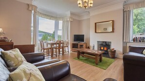 A living room with a fireplace, a television, and a dining area with a table and chairs. - 2 Bed in Cockermouth (oc-sz431) (Wythop)