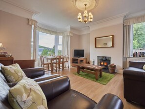 A living room with a fireplace, a television, and a dining area with a table and chairs. - 2 Bed in Cockermouth (oc-sz431) (Wythop)