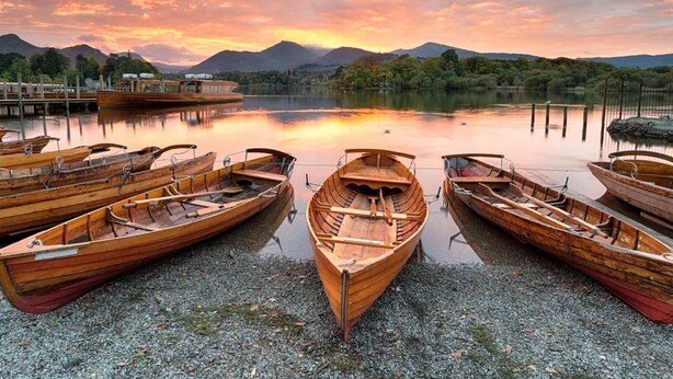 Wooden boats docked at a lakeside pier with mountains in the background. - 2 Bed in Cockermouth (oc-sz431) (Wythop)