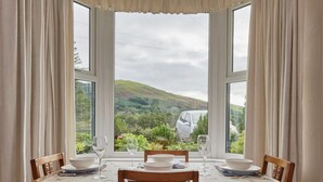 A dining table with chairs and a view of a car and hills through large windows. - 2 Bed in Cockermouth (oc-sz431) (Wythop)