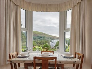 A dining table with chairs and a view of a car and hills through large windows. - 2 Bed in Cockermouth (oc-sz431) (Wythop)