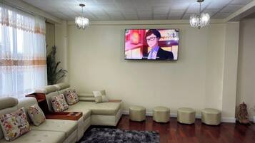 A living room with a sectional sofa, ottomans, a flat-screen TV, and a chandelier.