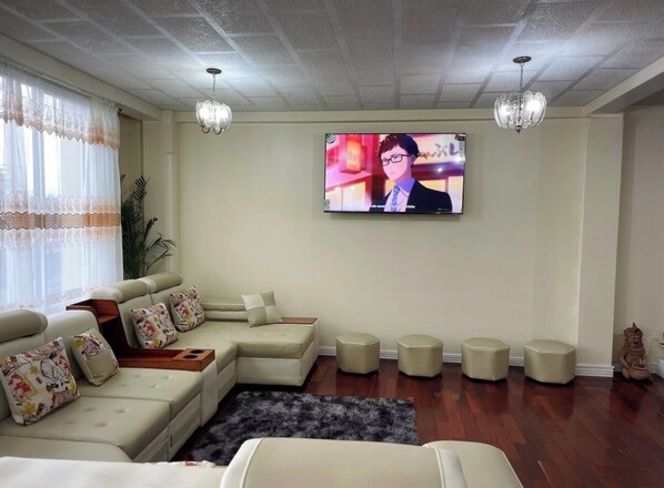 A living room with a sectional sofa, ottomans, a flat-screen TV, and a chandelier.
