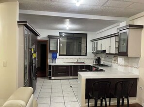 Una cocina compacta con una isla central, muebles oscuros y piso de baldosas.