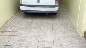 Ein weißer Volkswagen steht in einer schmalen, mit Fliesen belegten Auffahrt mit Metallüberdachung und gelben Wänden.