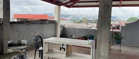 A covered outdoor area with a concrete bench, a grill, and chairs.