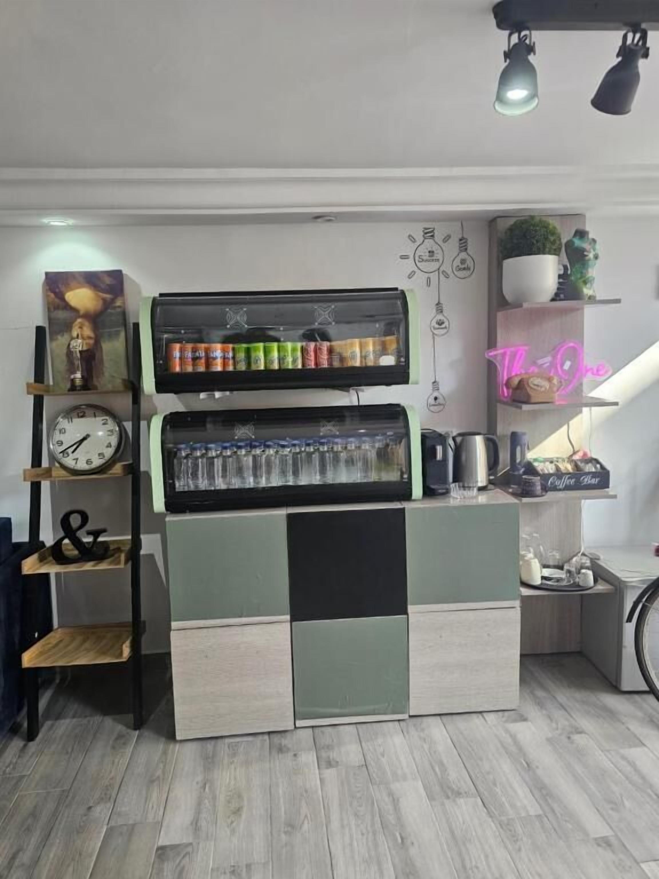 Une petite cuisine équipée d’une machine à café, d’étagères remplies de divers objets et d’un néon.
