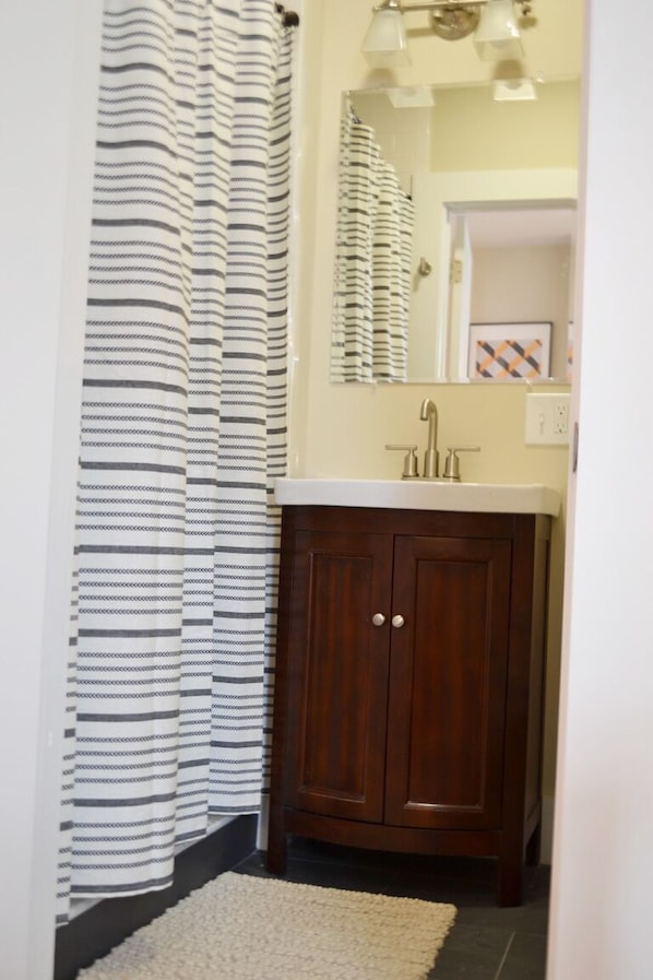 Een badkamer met een gestreept douchegordijn, een houten kastje, een witte wastafel en een spiegel boven de wastafel.