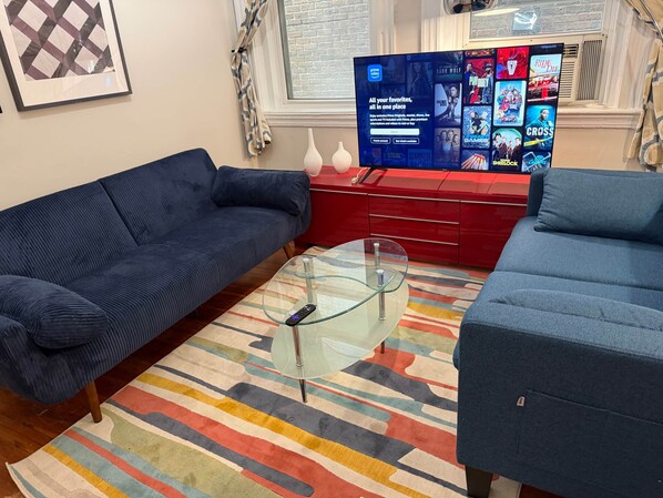 Un salon avec un canapé bleu, une table basse en verre et un meuble de télévision rouge sur lequel est posée une télévision affichant l’interface d’un service de diffusion en continu.