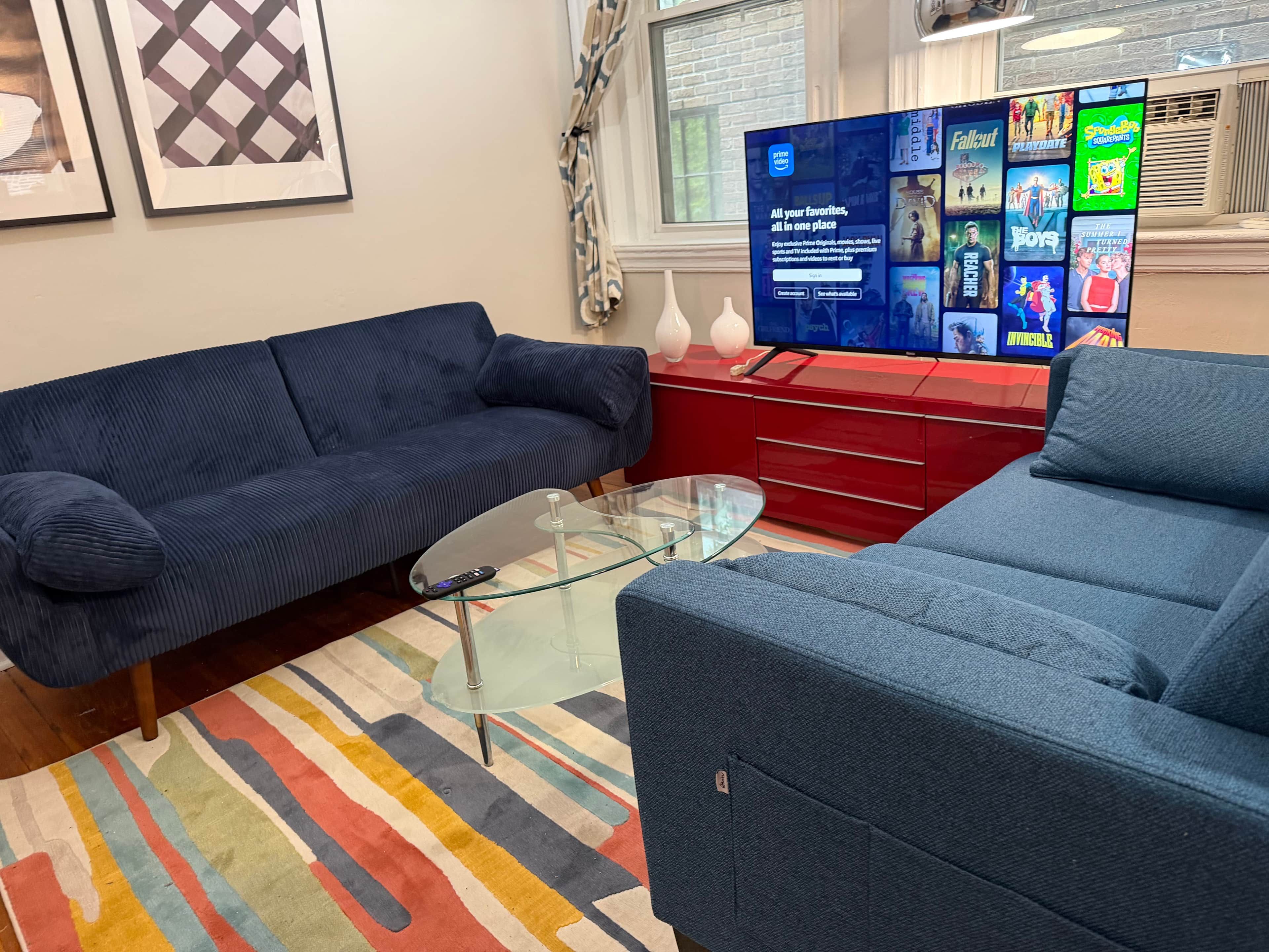 Ein Wohnzimmer mit einem blauen Sofa, einem Glastisch und einer roten Unterhaltungsanlage mit einem Fernseher, der Filmplakate zeigt.