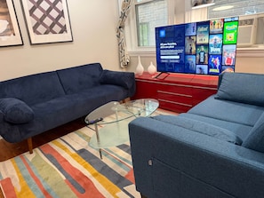 A living room with a blue sofa, a glass coffee table, and a red entertainment unit with a TV displaying movie posters.