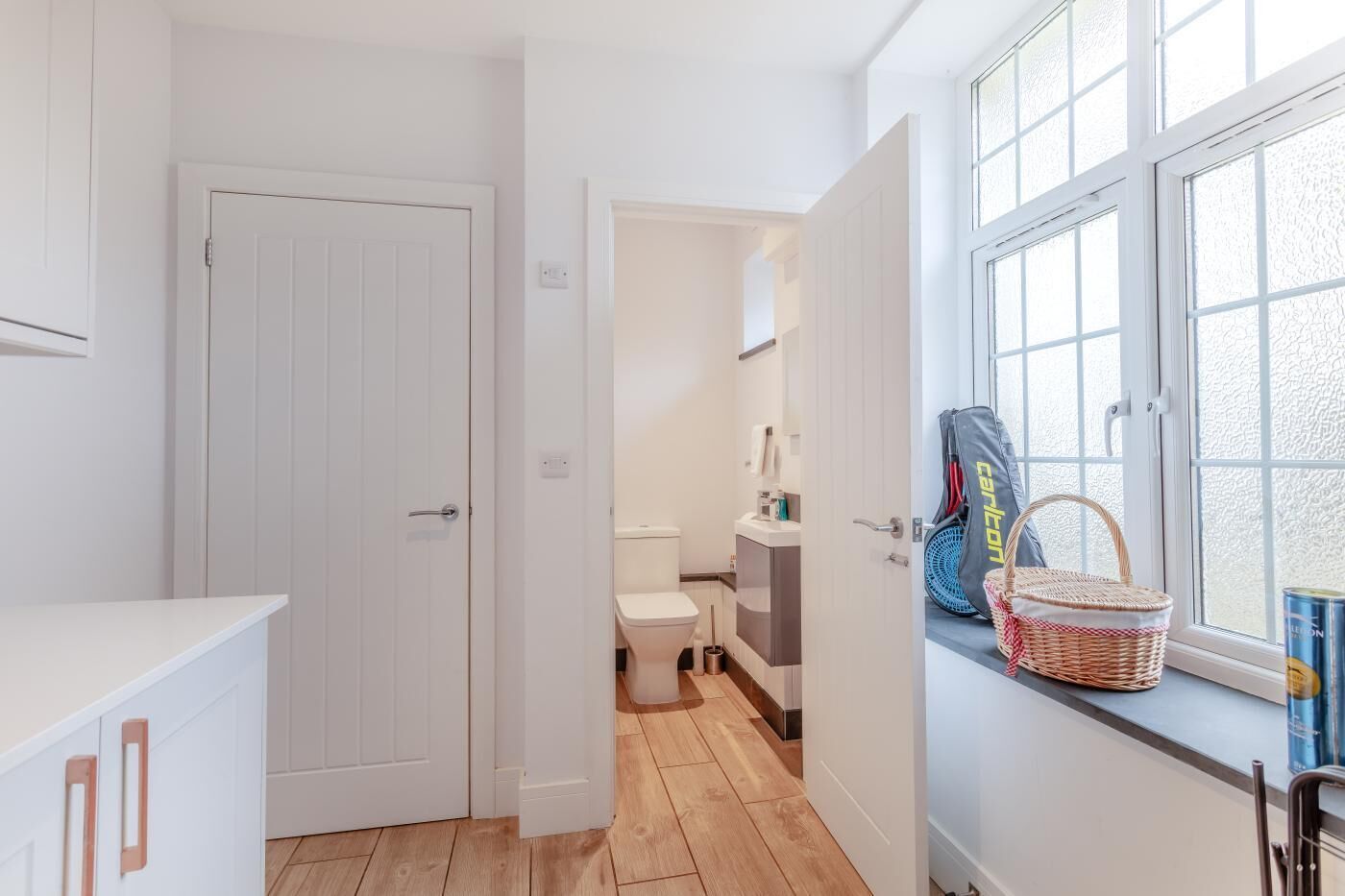 A compact bathroom with a toilet, a small sink, and a window with a basket and bag.